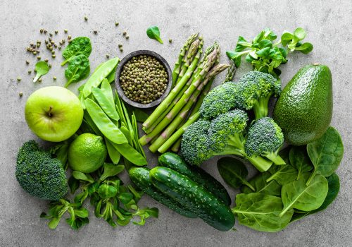 Healthy vegetarian food concept background, fresh green food selection for detox diet, raw broccoli, apple, cucumber, spinach, peas, asparagus, avocado, lime, corn salad and mung bean, view from above, flat lay
