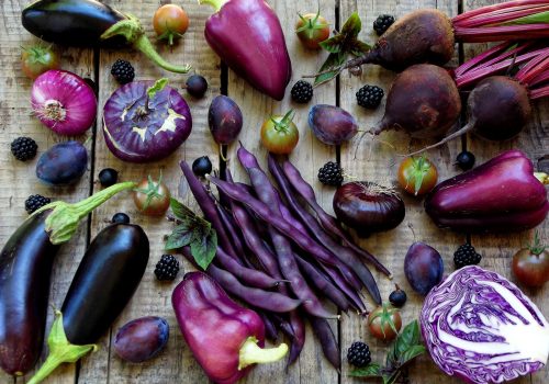 purple vegetables and fruits on wooden background - eggplant, cauliflower, green beans, cherry tomatoes, plum, basil, onion, cabbage, sweet pepper